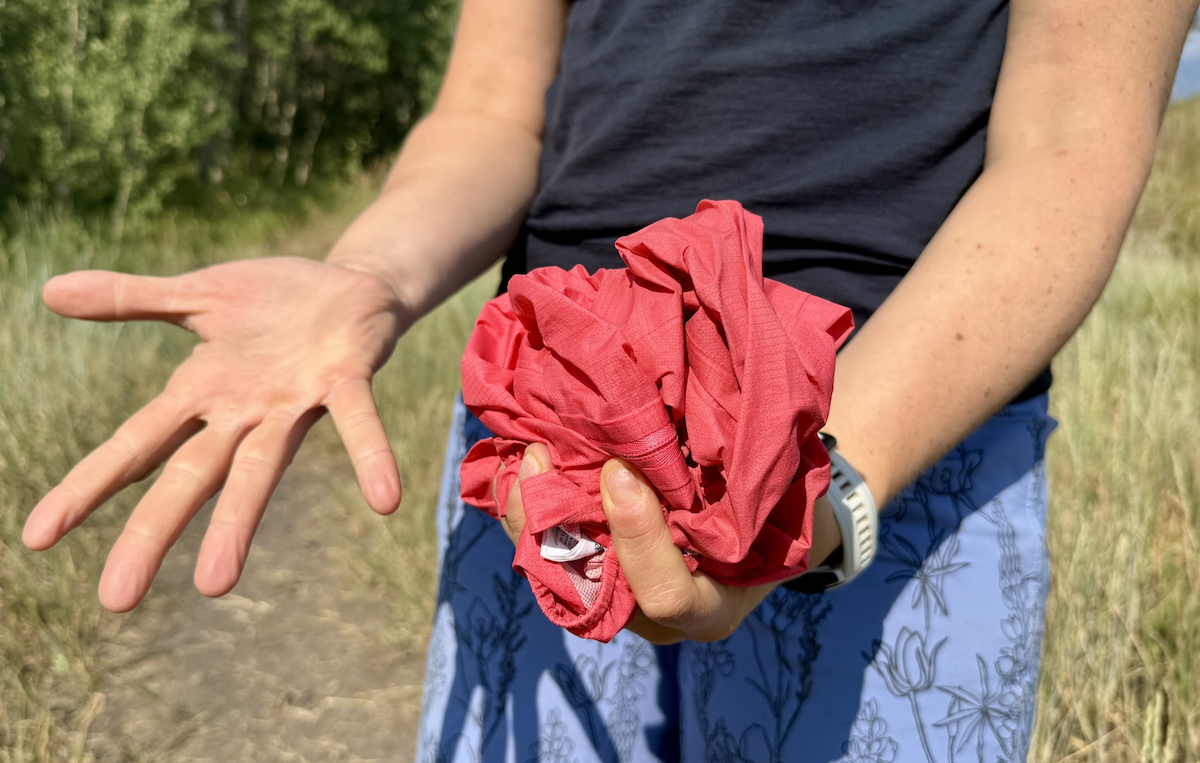 a woman's hands hold a pink packable rain jacket to show how small it is