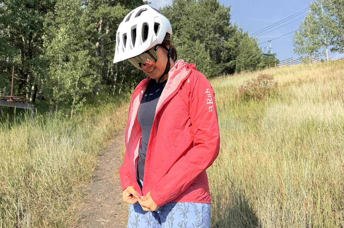 a woman zips up a pink rain jacket on a bike ride