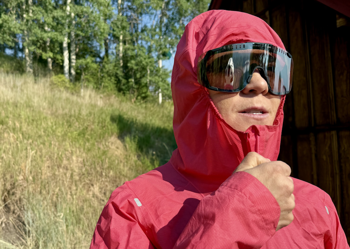  a woman zips up a rain jacket on a very sunny day