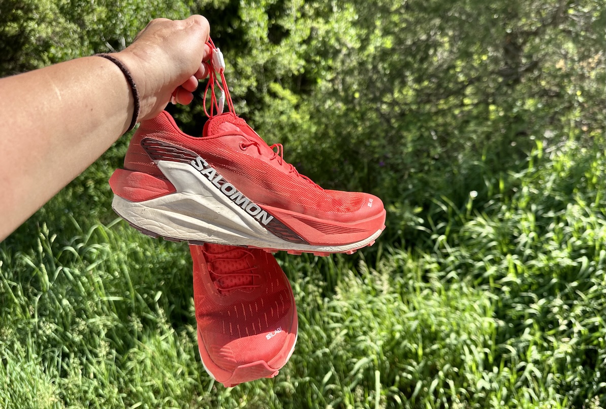a hand holding red running shoes against foliage 