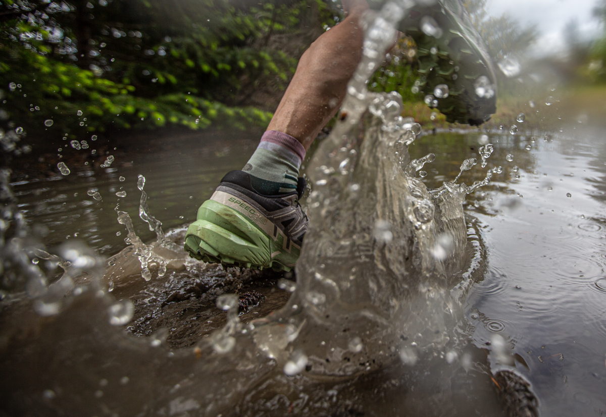 A close up of running shoes splashing through muddy puddle