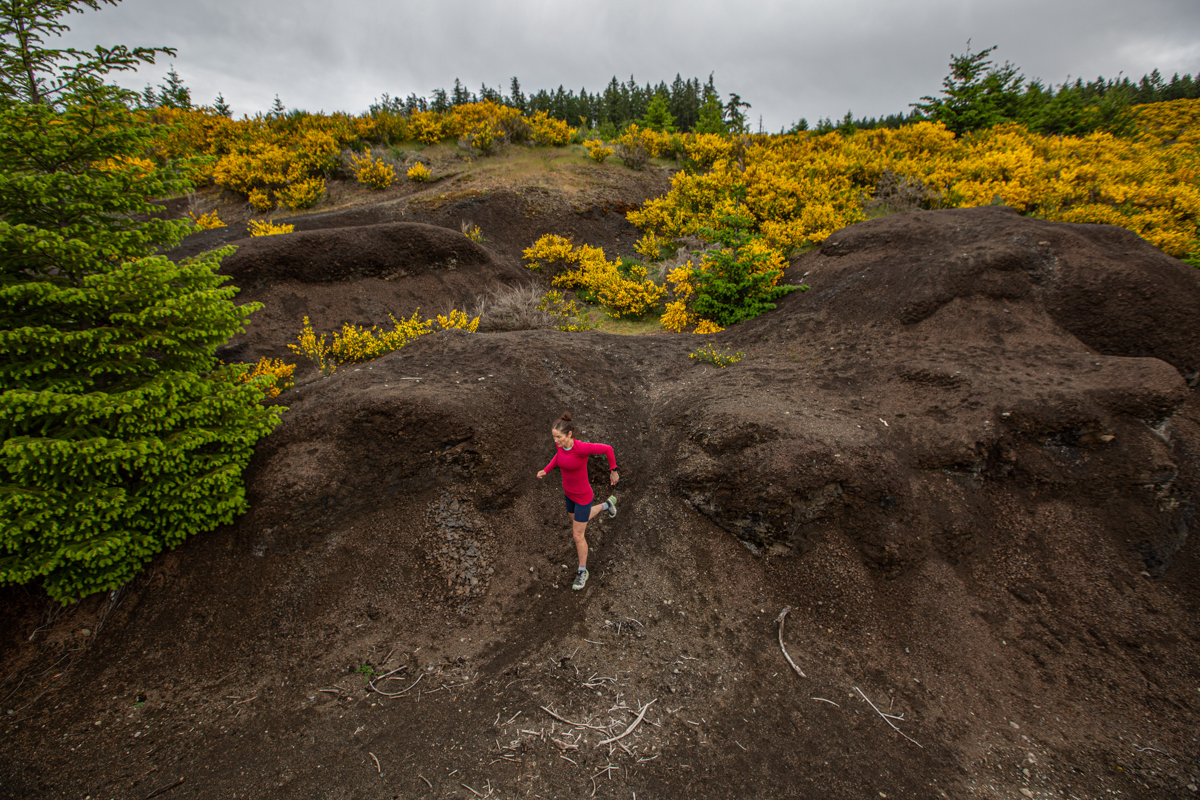 A woman running down a steep and muddy bike trail in trail running shoes
