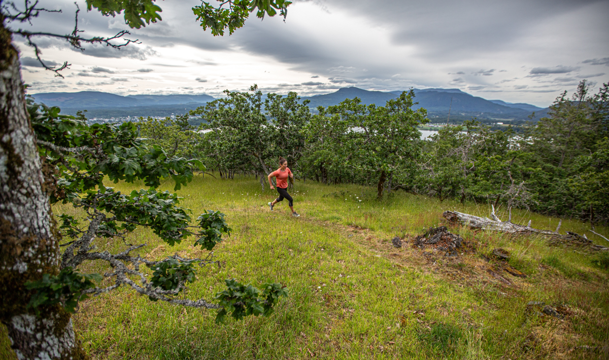 A woman running through grassy trail in trail running shoes