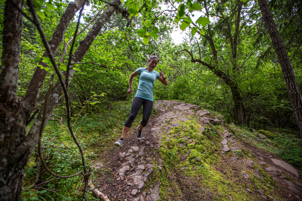 A woman running over rocky and uneven forest terrain in trail running shoes