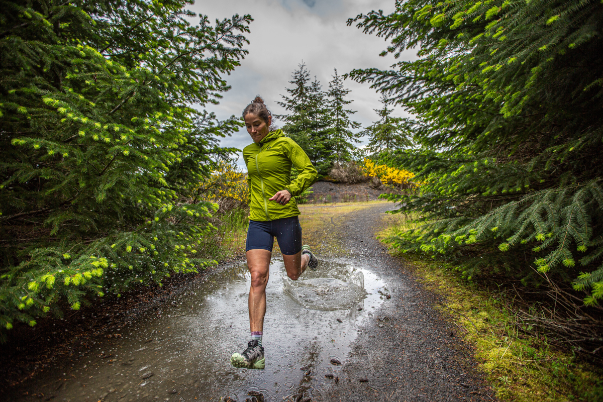 A woman running through mud puddle in forest with trail running shoes 