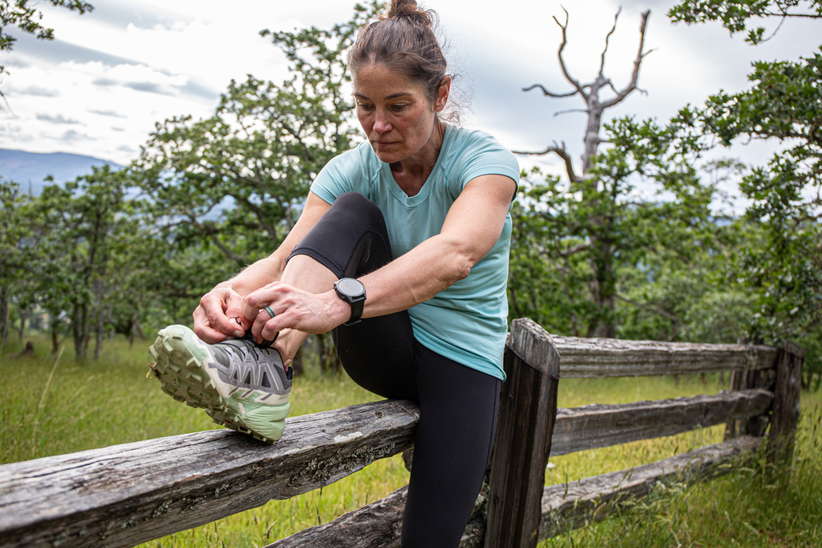 Woman putting on trail running shoes while leaning on fence