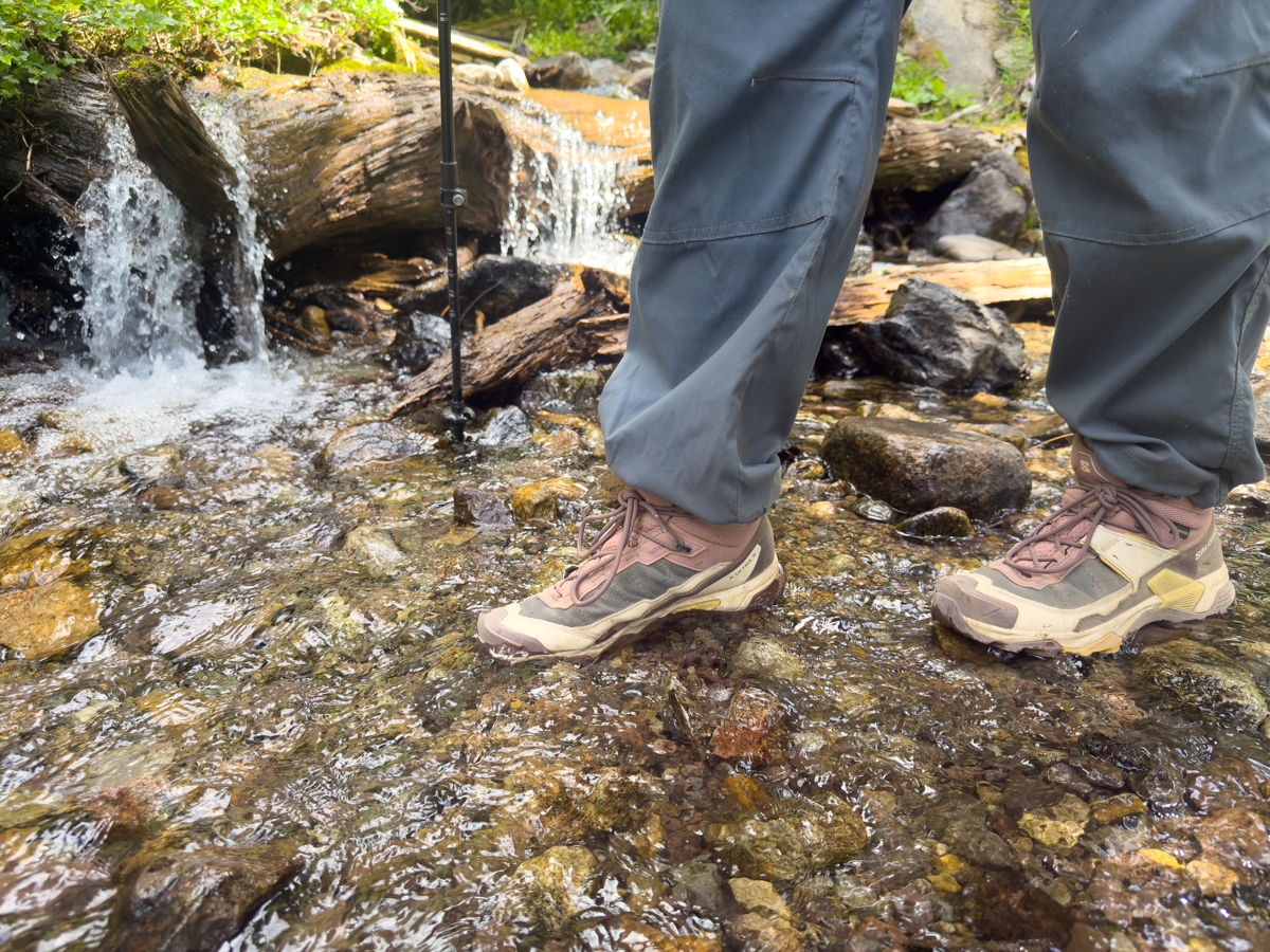 A pair of brown and pink hiking boots walking across a stream