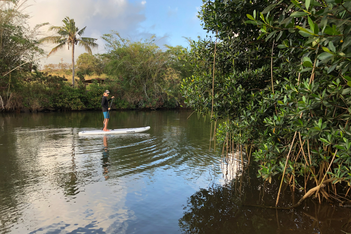 A man paddling in the distance on flat water at sunset