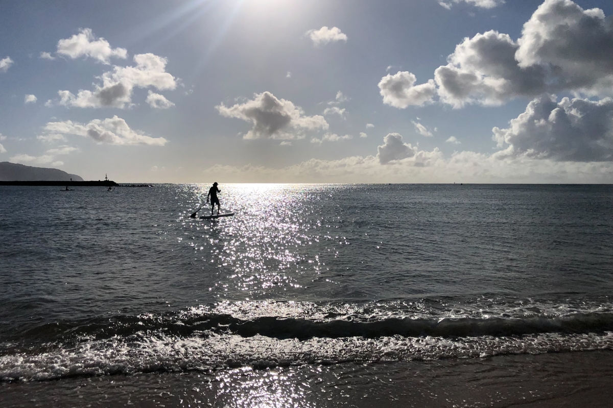 A silhouette of a man paddling on a board in the ocean at sunset