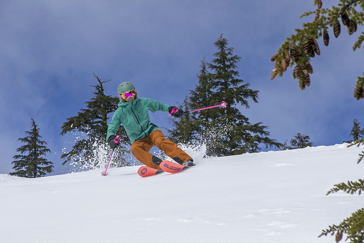 A woman skies toward the camera in powder with trees in the background