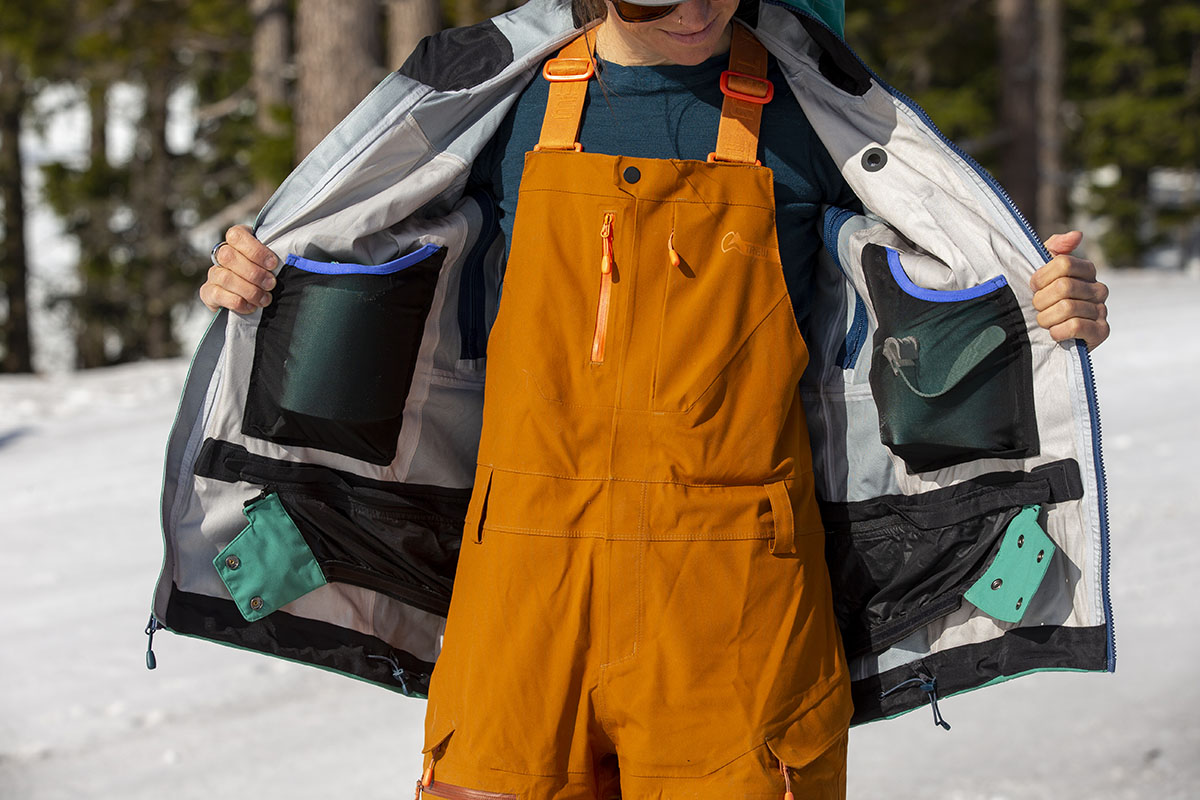 A skier holds open her ski jacket to show the interior pockets and powder skirt
