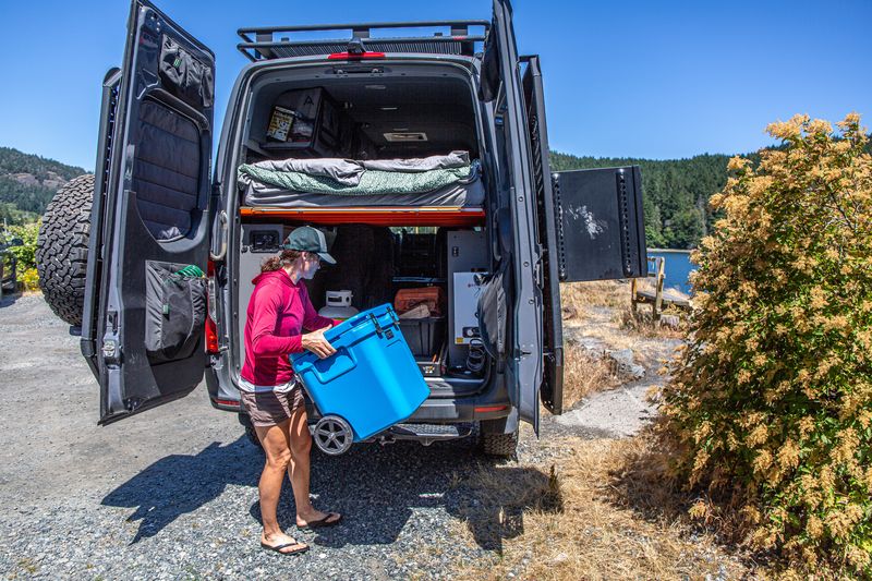A woman loads a cooler into a tall van