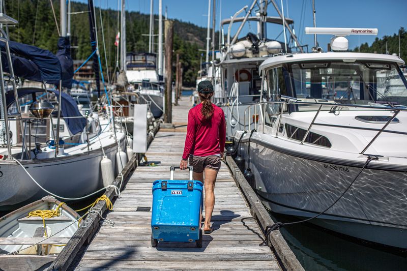 A woman pulls a wheeled cooler down a boat dock
