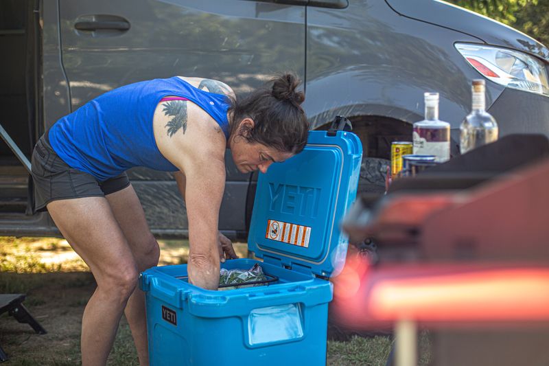 A woman bends over and unloads gear from a blue cooler