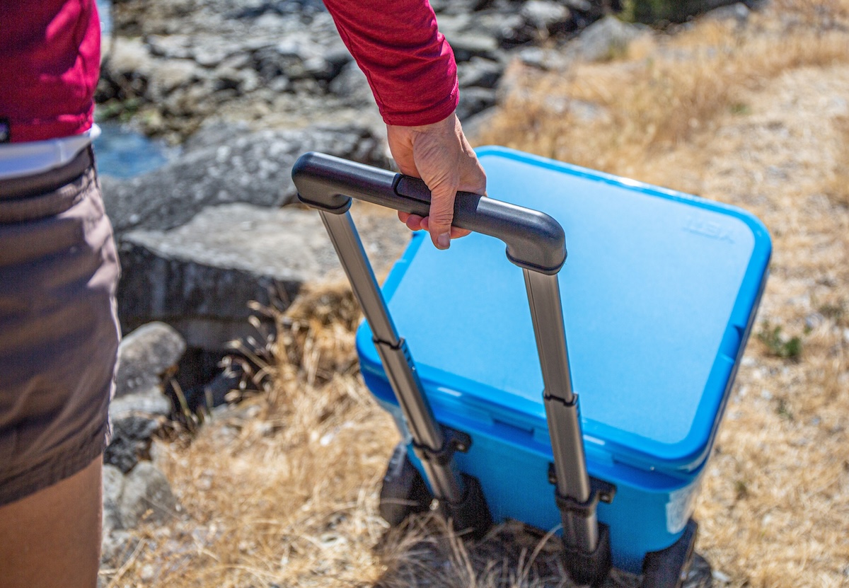 A woman pulls a wheeled cooler by the handle