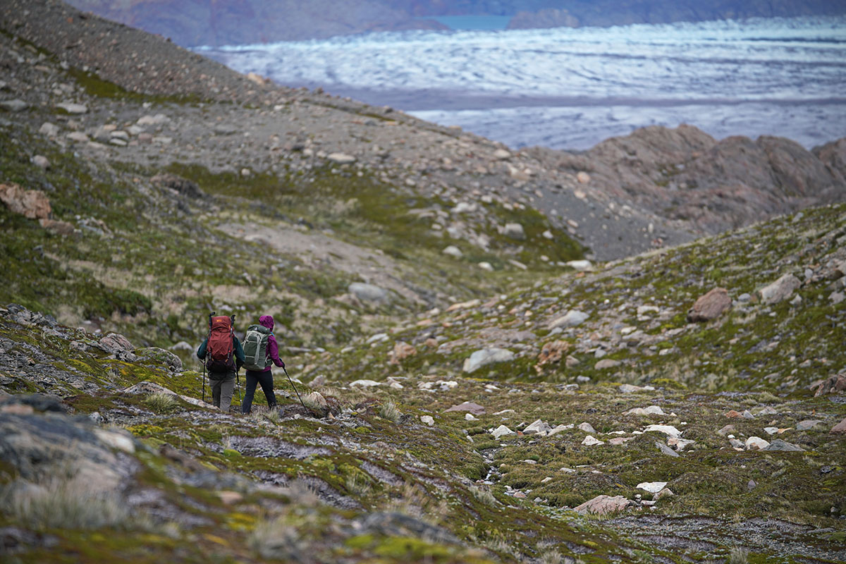 Two hikers make their way down a rocky path in the distance.