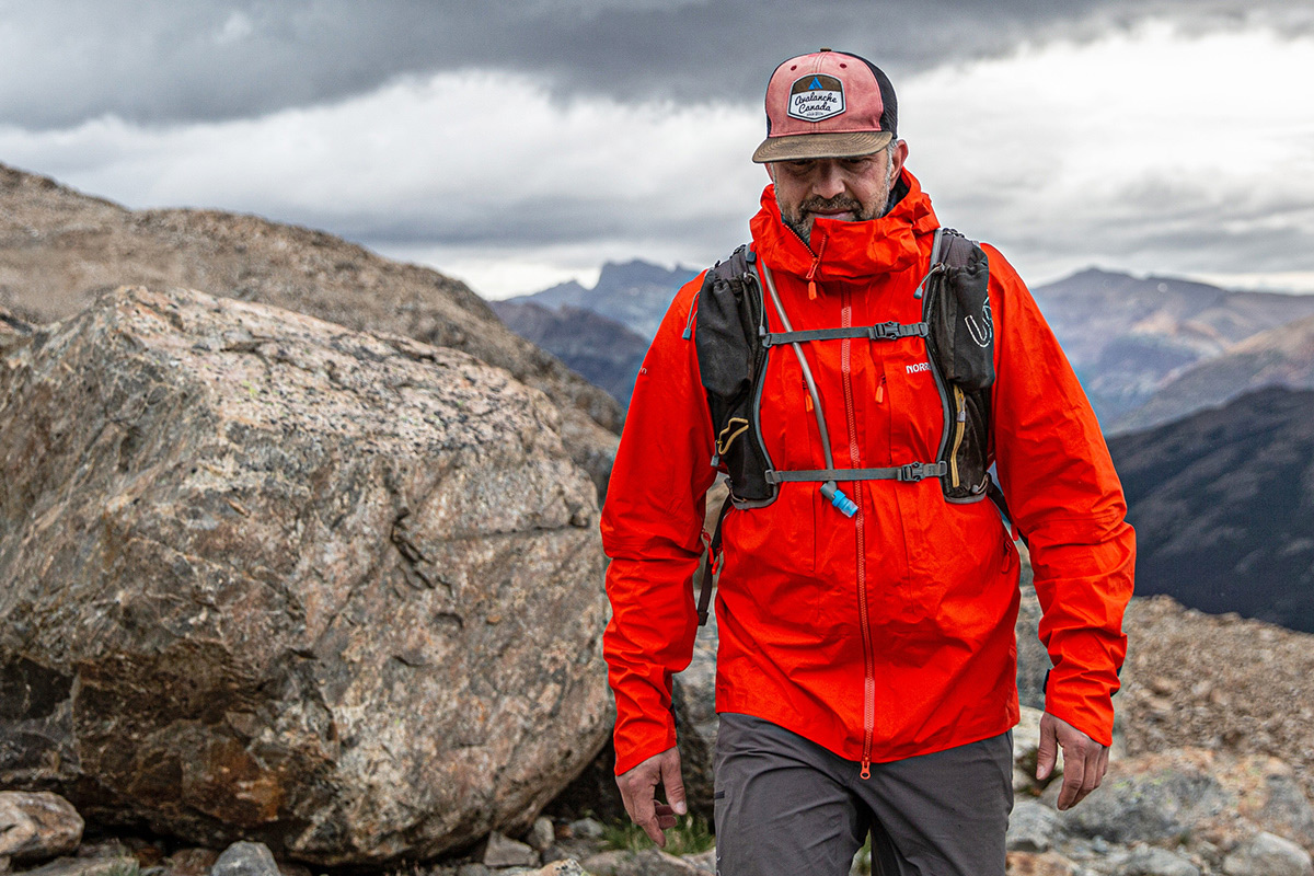 A man walks over a steep mountain ridge in a red Norrona jacket.