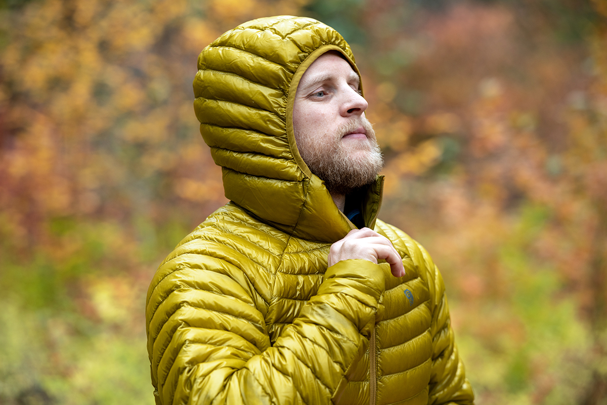 A hiker zips up his bright yellow jacket while glancing at the fall leaves. 