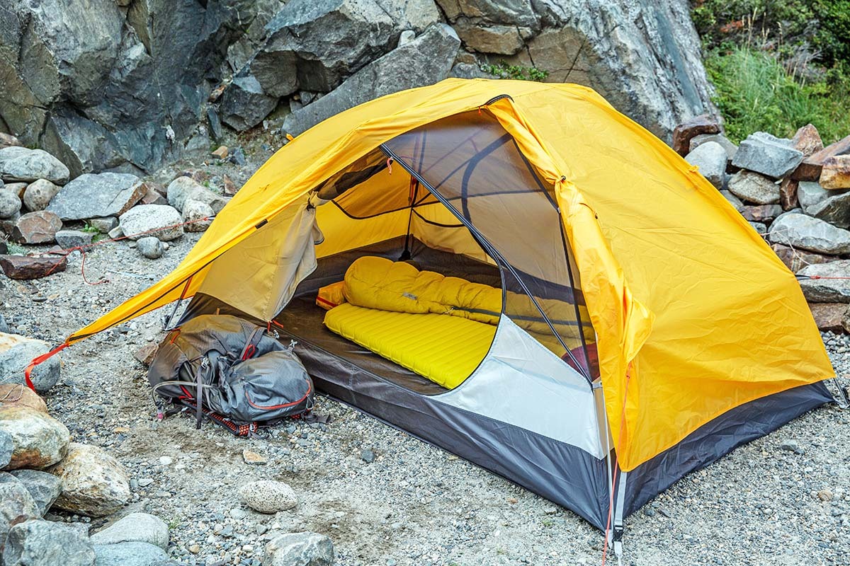 A yellow REI backpacking tent pitched on rocky ground