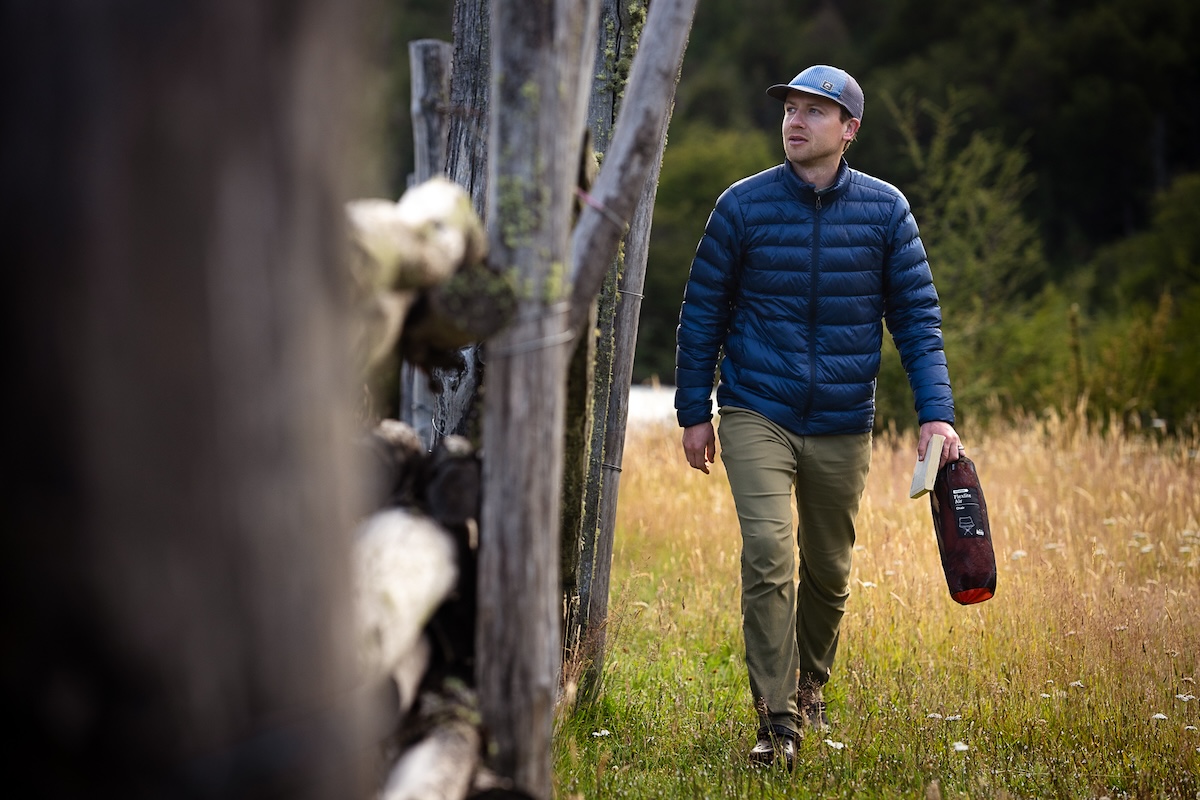 A man walks around the side of his cabin in a down jacket.