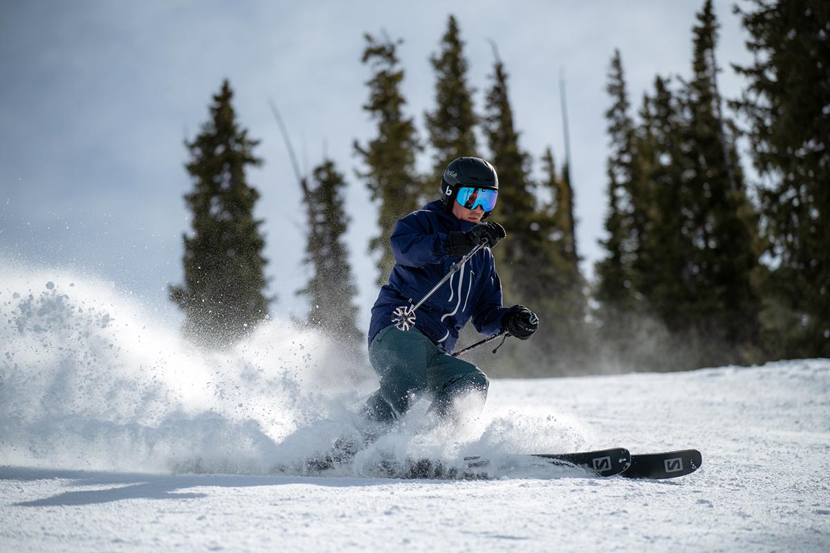 A skiier sprays powder while skiing down a sunny slope.