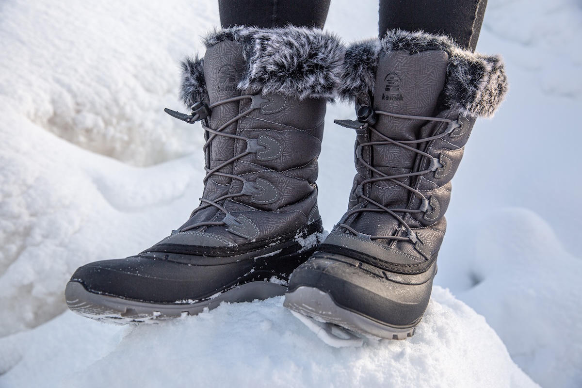 A close up of a grey pair of Kamik winter boots standing on a mound of snow