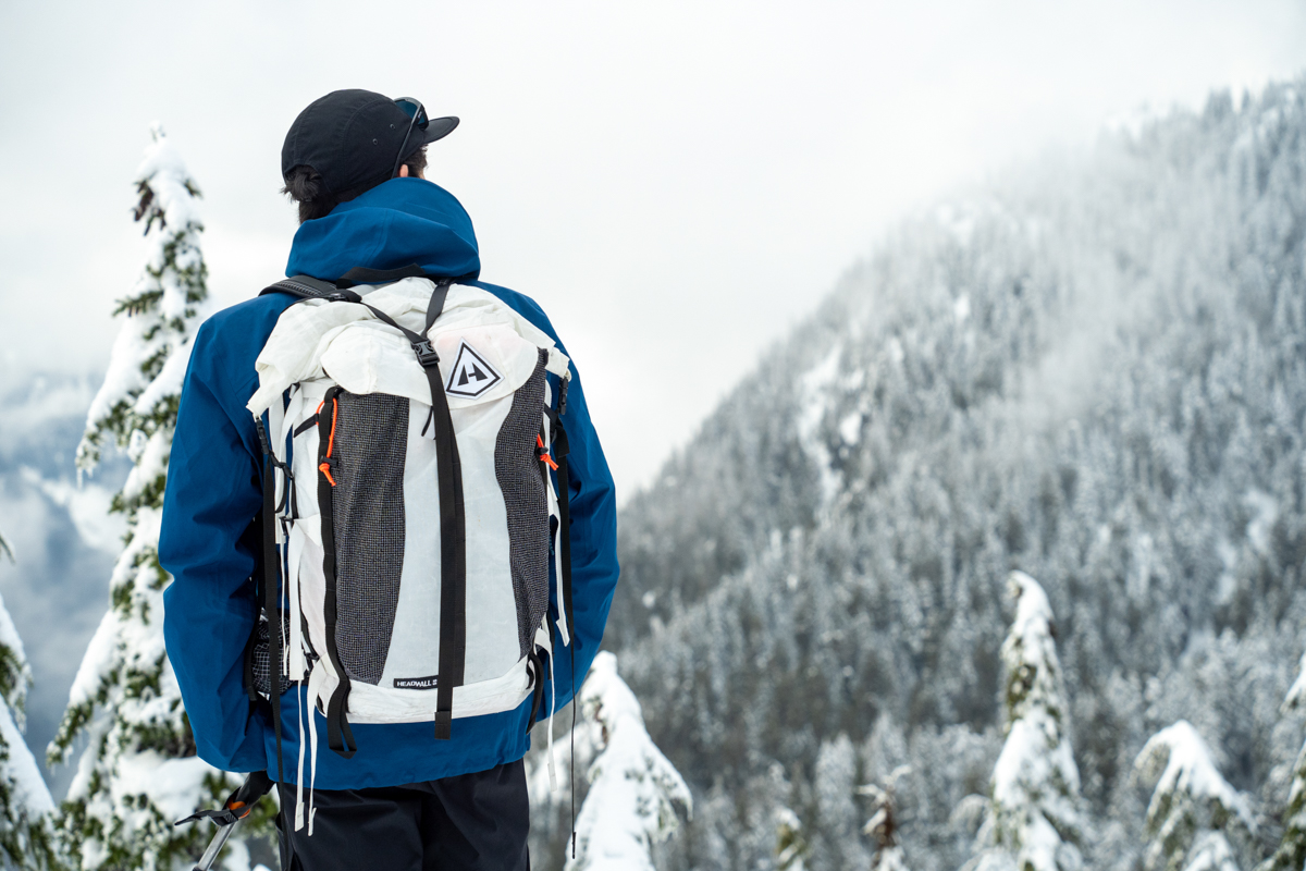 A man wearing a large white ski backpack in a snowy forest