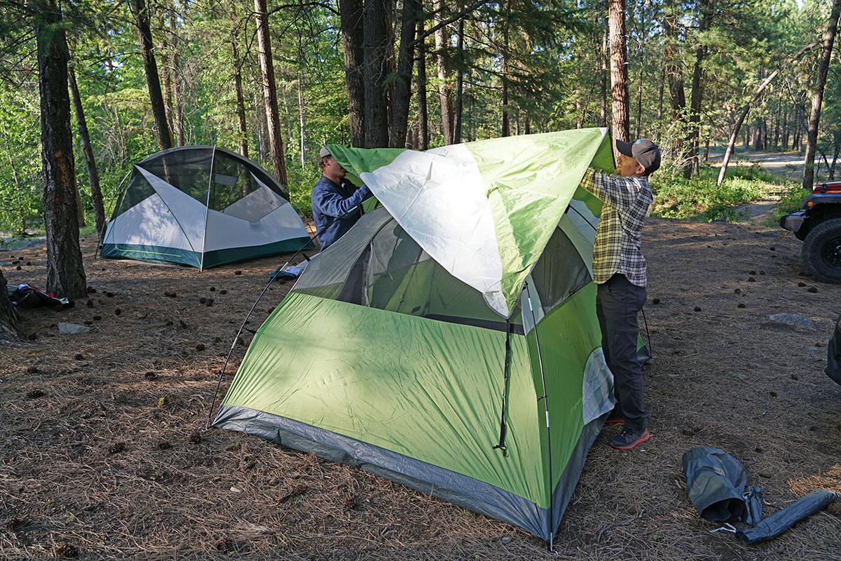 Two campers work to set up a rainfly over top of their camping tent.