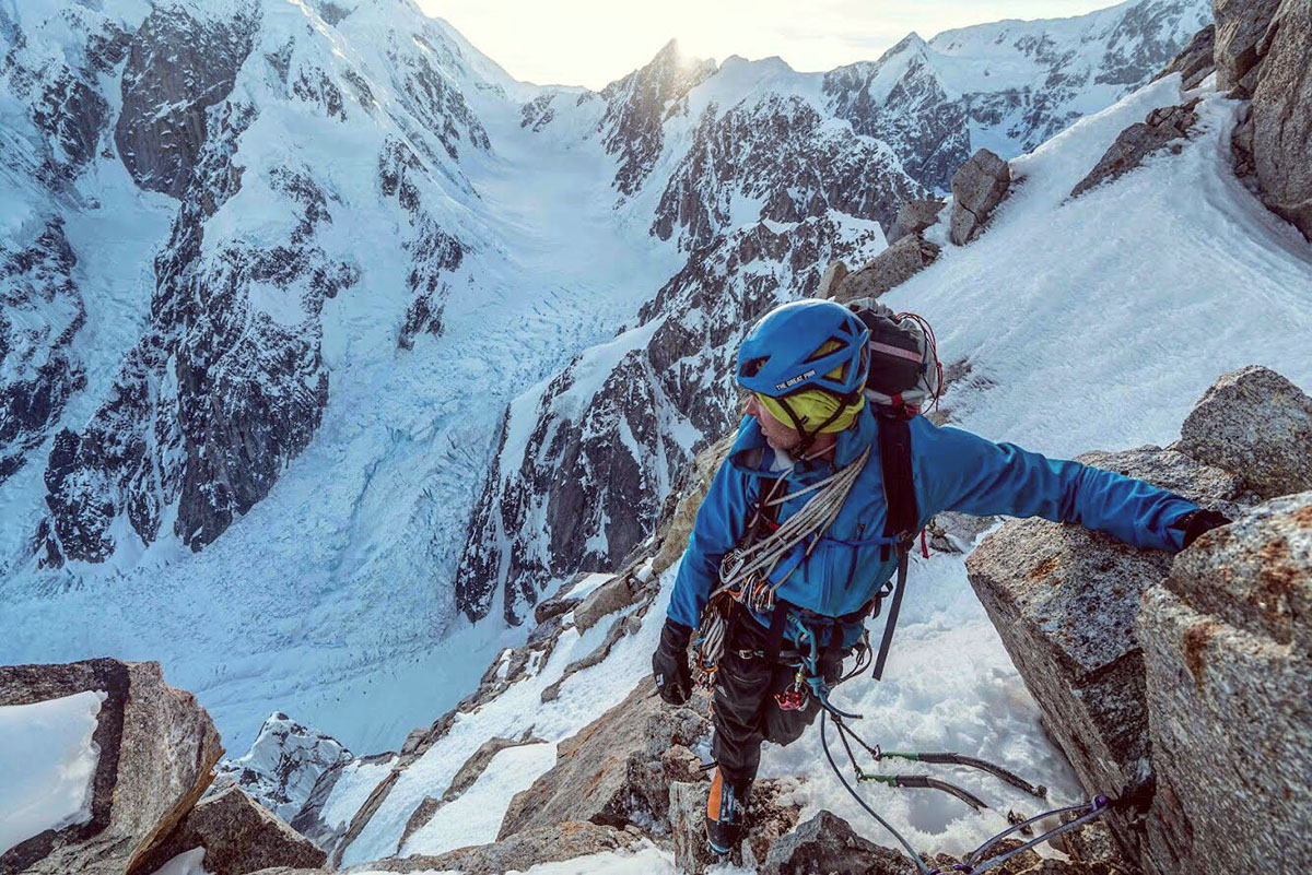 A mountaineer is perched on a rock near the summit of an icy peak. 
