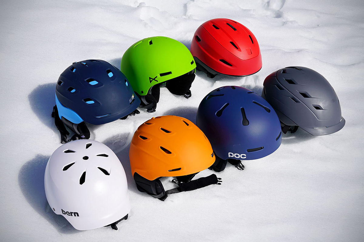 Seven helmets of various colors next to each other on the snow