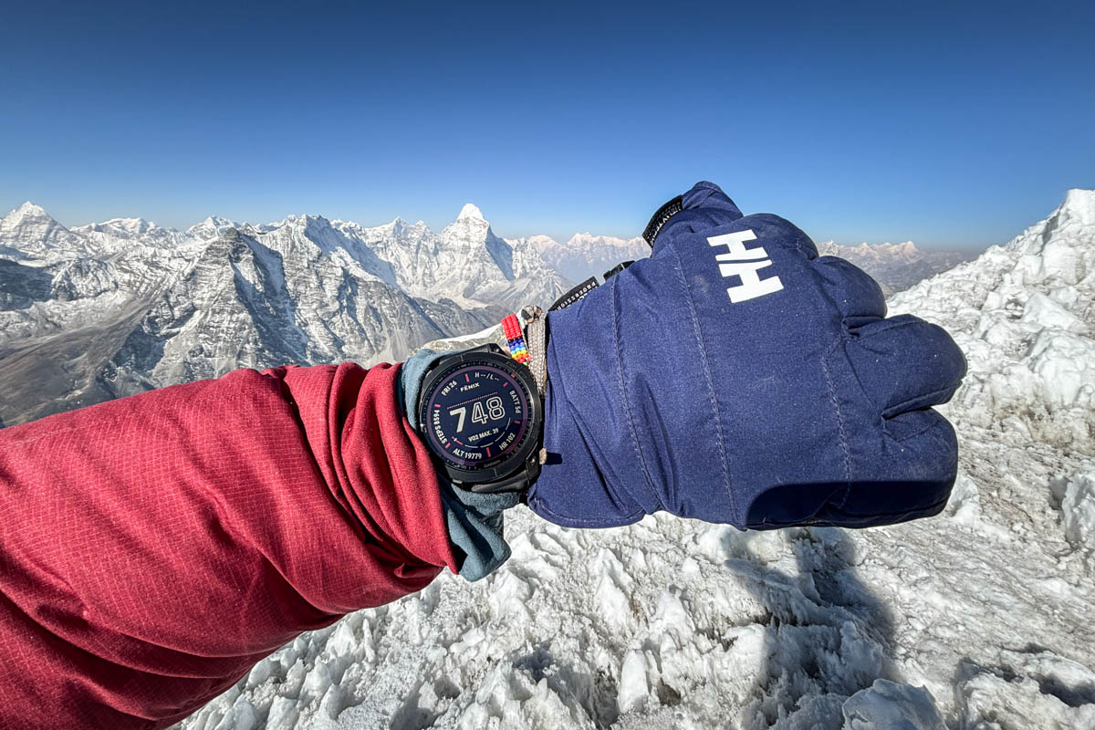 A closeup of a wrist with the Garmin Fenix 7 with snowy mountain peaks in the background