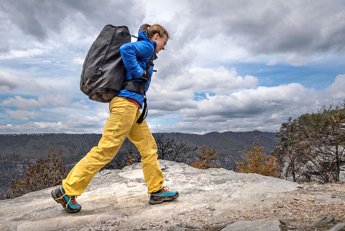 A woman hikes across a rock slab with a big pack, wearing the La Sportiva TX3 approach shoes