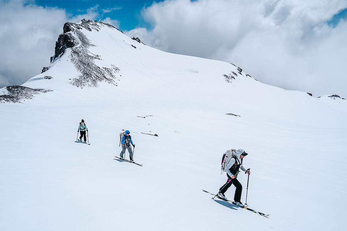 A group of skiiers climb a steep, snowy peak in the mountains.
