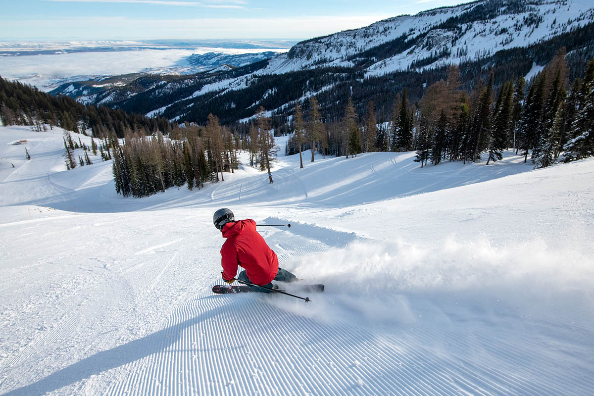 A man skis downhill at a ski resort in the mountains.