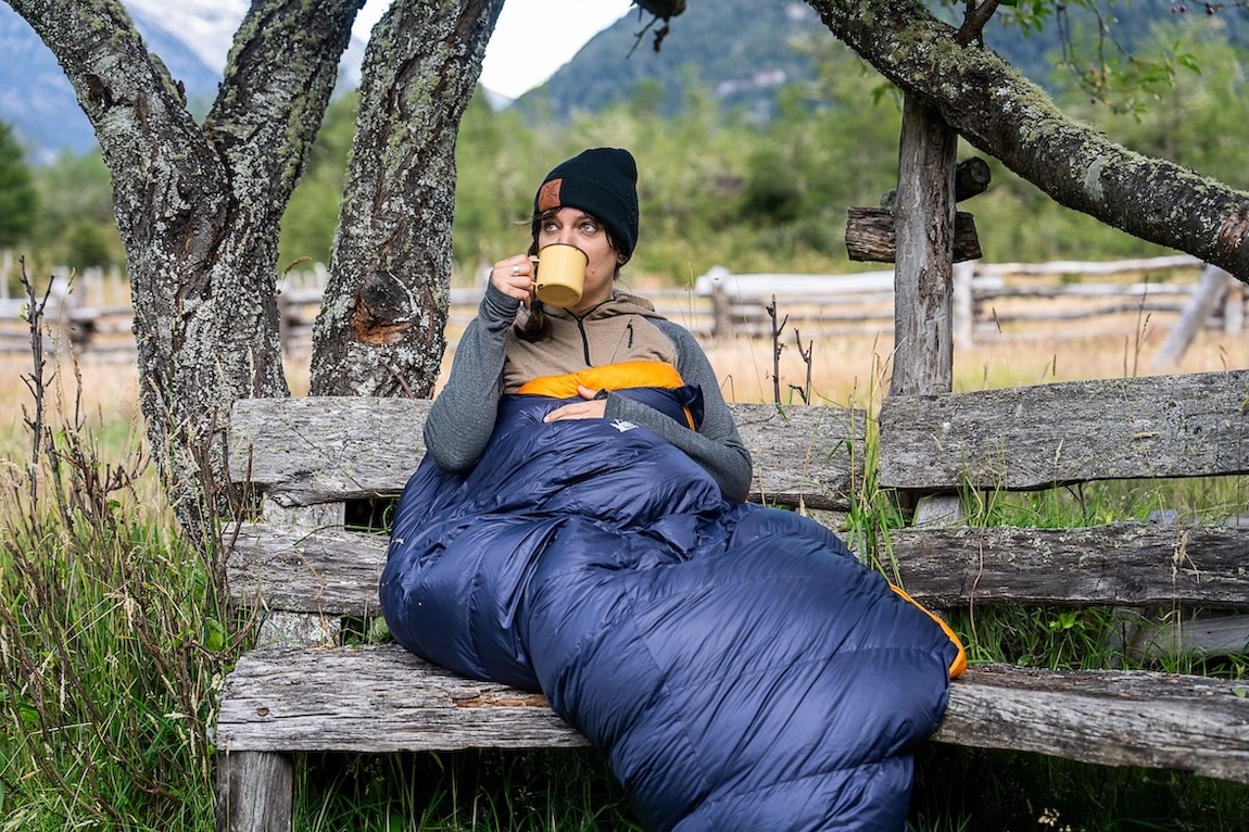 A woman enjoying a cup of coffee while tucked inside a sleeping bag