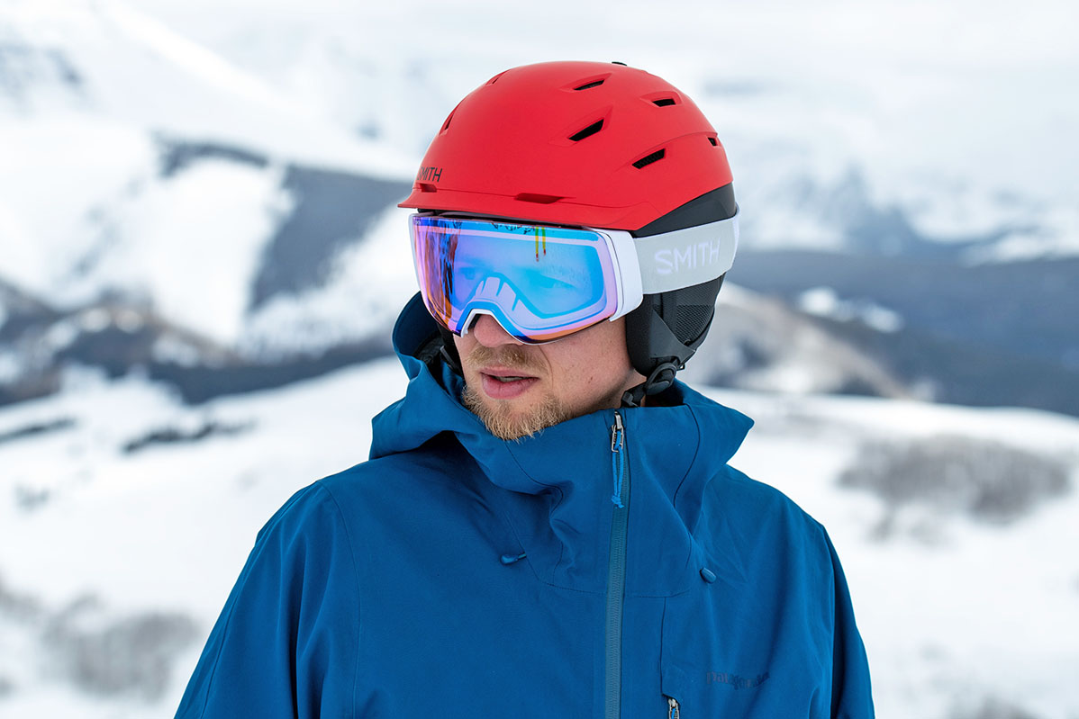A skier wears a bright red ski helmet on a snowy mountain top.