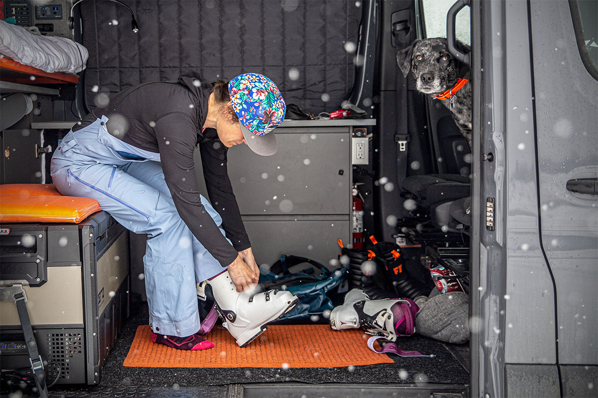 A woman sitting down inside a van tightens up her ski boots