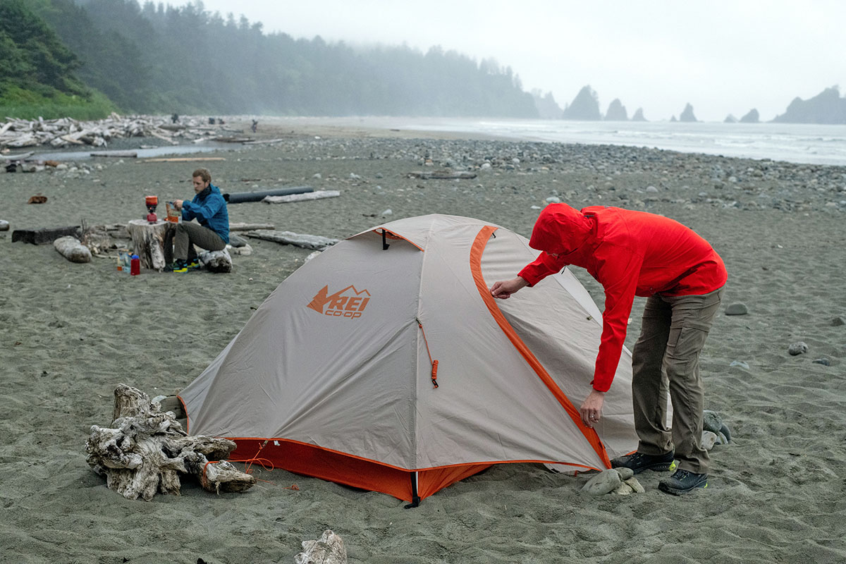 A camper zips up a tent on a misty afternoon in the mountains.