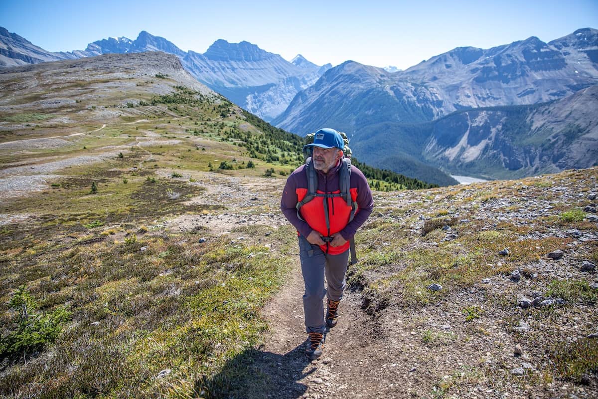 A man hikes on a mountain trail in a brightly colored fleece jacket
