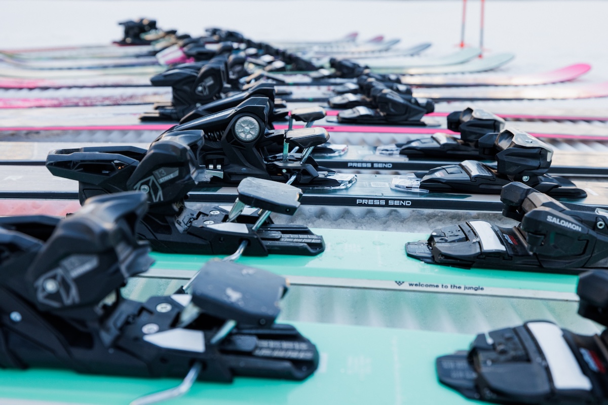 A close up of the bindings on a bunch of skis lined up in the snow