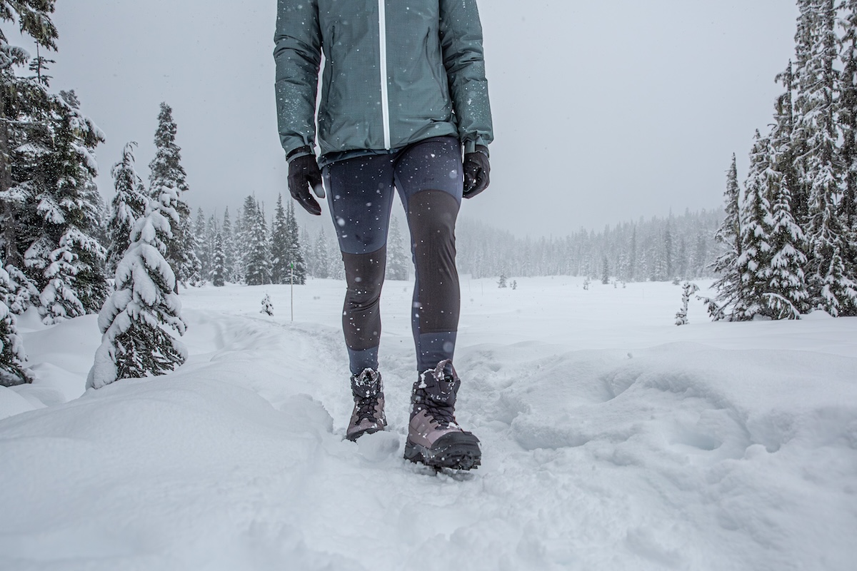 A woman walks along a snowy trail on a grey and stormy day