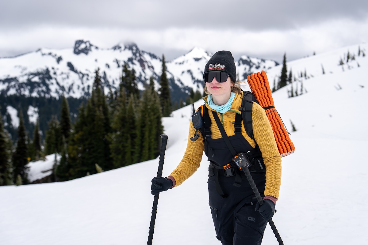 A smiling woman skins up on Mt. Rainier wearing ski bibs