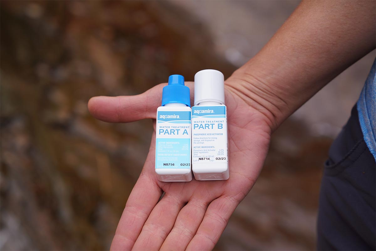 A hand holding Aquamira water treatment bottles