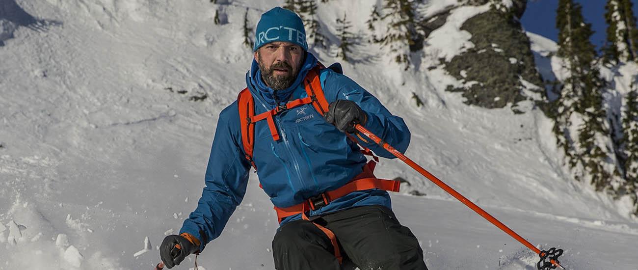 A man skis down a slope toward the camera in a blue jacket