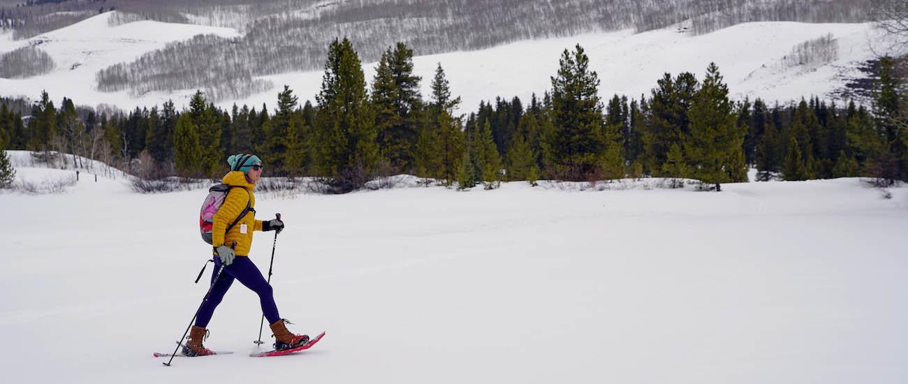 A woman walks across a snowy expanse on snowshoes