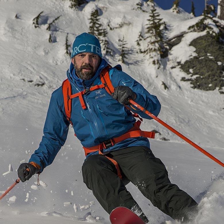A man skis down a slope toward the camera in a blue jacket