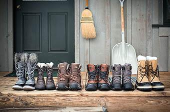 A lineup of six different kinds of winter boots set out on a porch