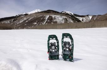 A pair of showshoes stick out of the snow with mountains in the background